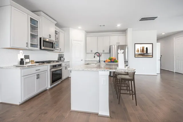 a kitchen with stainless steel appliances a stove top oven a sink a refrigerator white cabinets and wooden floor