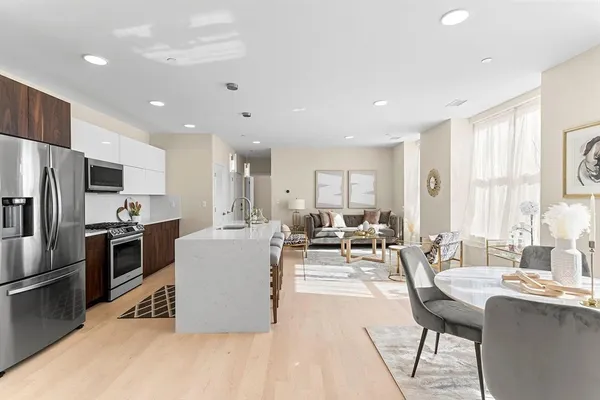 a living room with stainless steel appliances kitchen island granite countertop a table chairs and a refrigerator