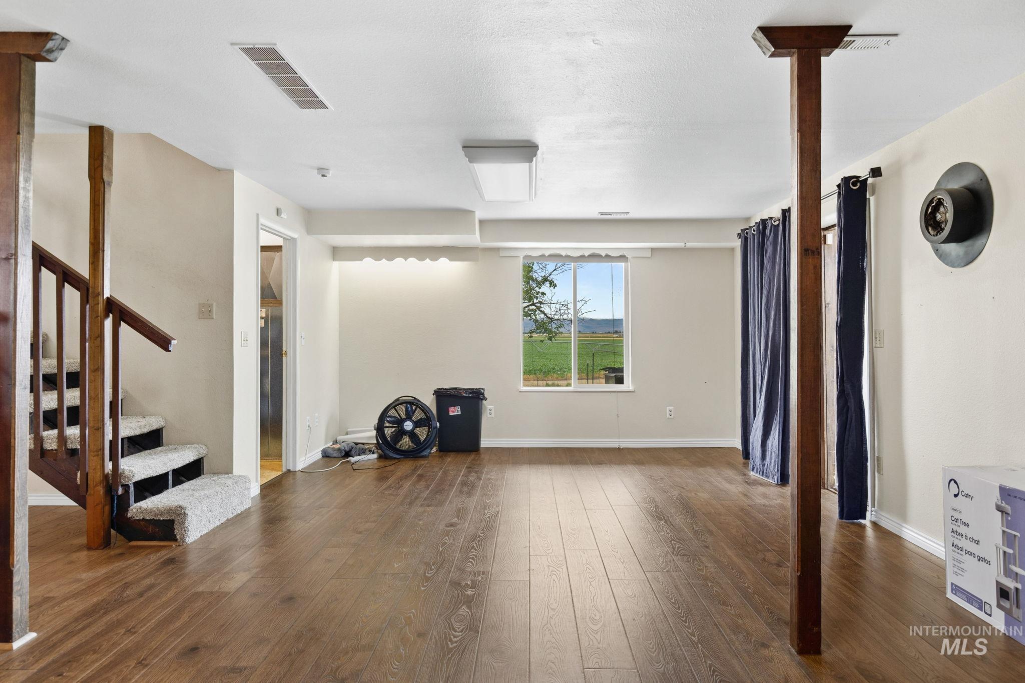 18338 Pride Lane Caldwell, ID 83607 - Photo 17 of 50 Spacious room featuring wood-finish flooring, a window offering an expansive outdoor scene, and a carpeted staircase with wood railing