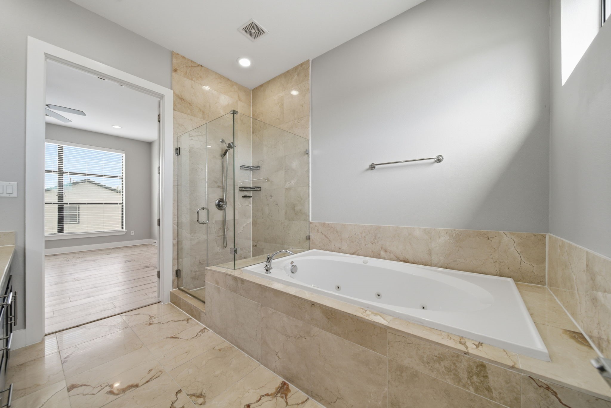 1814 Thompson Street Houston, TX 77007 - Photo 11 of 37 Modern primary bathroom showcasing a sleek, upscale design with marble tile flooring and wall accents. A spacious glass-enclosed shower and elegant built-in soaking tub create a spa-like retreat. Seamlessly connected to a bright primary bedroom featuring warm wood flooring and large windows that fill the space with natural light.