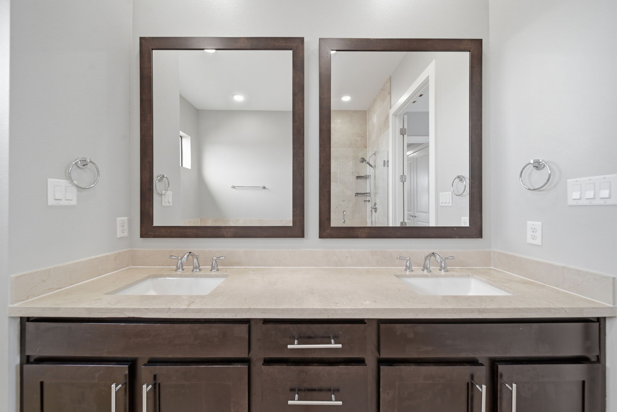 1814 Thompson Street Houston, TX 77007 - Photo 12 of 37 Modern bathroom featuring a dual-sink vanity with sleek natural stone countertops and rich dark wood cabinetry. Oversized framed mirrors enhance the sense of space, while soft neutral gray tones create a clean, spa-like atmosphere. The glass-enclosed, tiled shower adds a polished finishing touch, delivering a refined and contemporary feel.