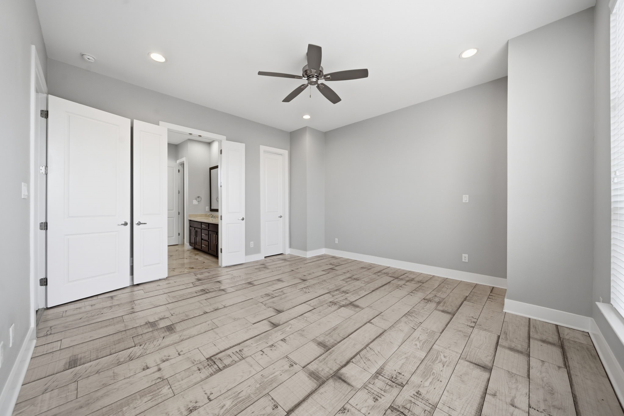1814 Thompson Street Houston, TX 77007 - Photo 13 of 37 Spacious and light-filled primary bedroom featuring modern wood flooring, soft neutral gray tones, and elevated finishes throughout. Large windows bring in abundant natural light, complemented by recessed lighting and a ceiling fan for year-round comfort. Double doors lead to a private en-suite bath, creating a seamless and functional retreat.