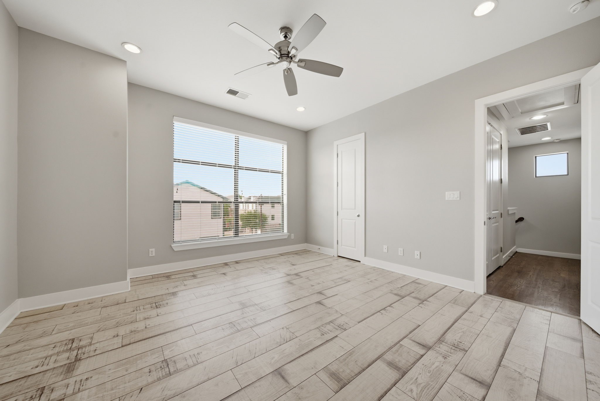 1814 Thompson Street Houston, TX 77007 - Photo 16 of 37 Bright and spacious primary suite featuring modern wood-look flooring, soft neutral tones, and a large window that fills the space with natural light. Designed for comfort and relaxation, this inviting retreat offers a clean, contemporary feel with a warm and airy atmosphere.