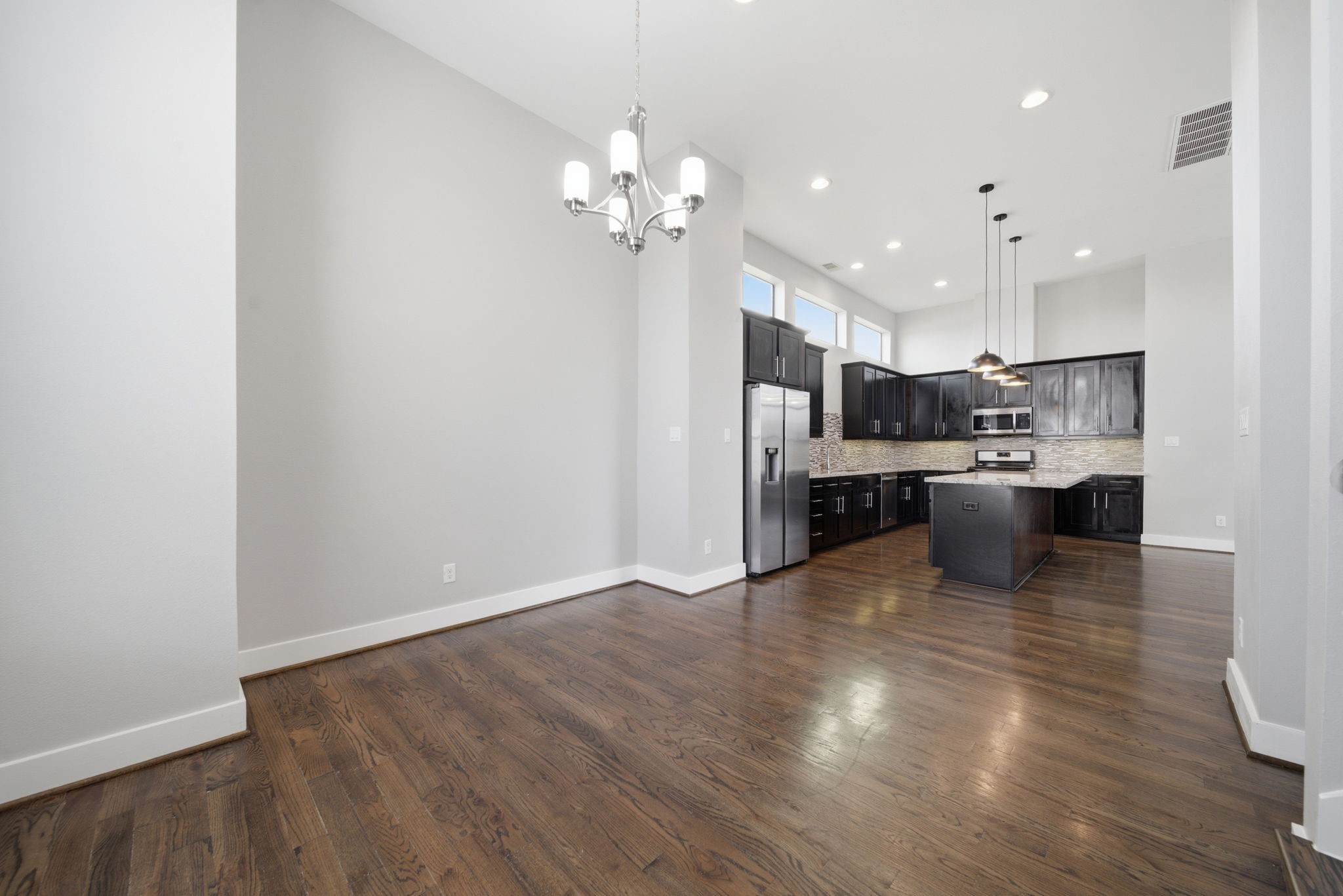 1814 Thompson Street Houston, TX 77007 - Photo 18 of 37 Stunning modern kitchen and dining area with high ceilings, rich dark wood flooring, and bold black cabinetry. A spacious island with pendant lighting anchors the space, complemented by stainless steel appliances and large windows that fill the home with natural light.