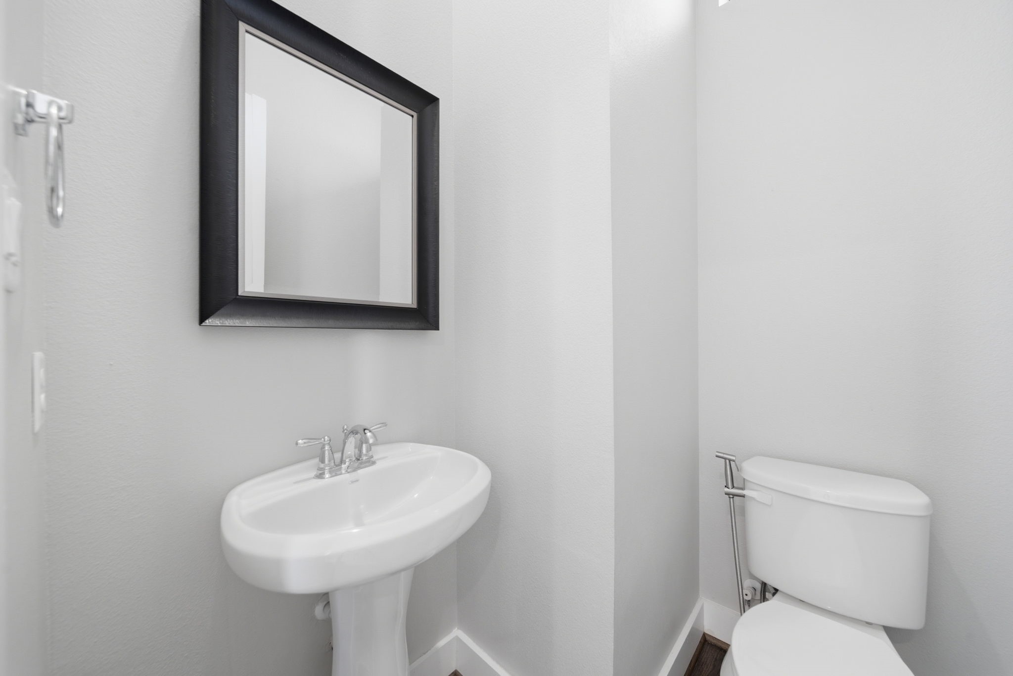 1814 Thompson Street Houston, TX 77007 - Photo 19 of 37 Modern, well-appointed half-bath featuring a sleek pedestal sink, framed mirror, and updated toilet. Clean, minimalist design with neutral tones creates a bright, polished space that feels fresh and inviting—perfect for guests and everyday convenience.