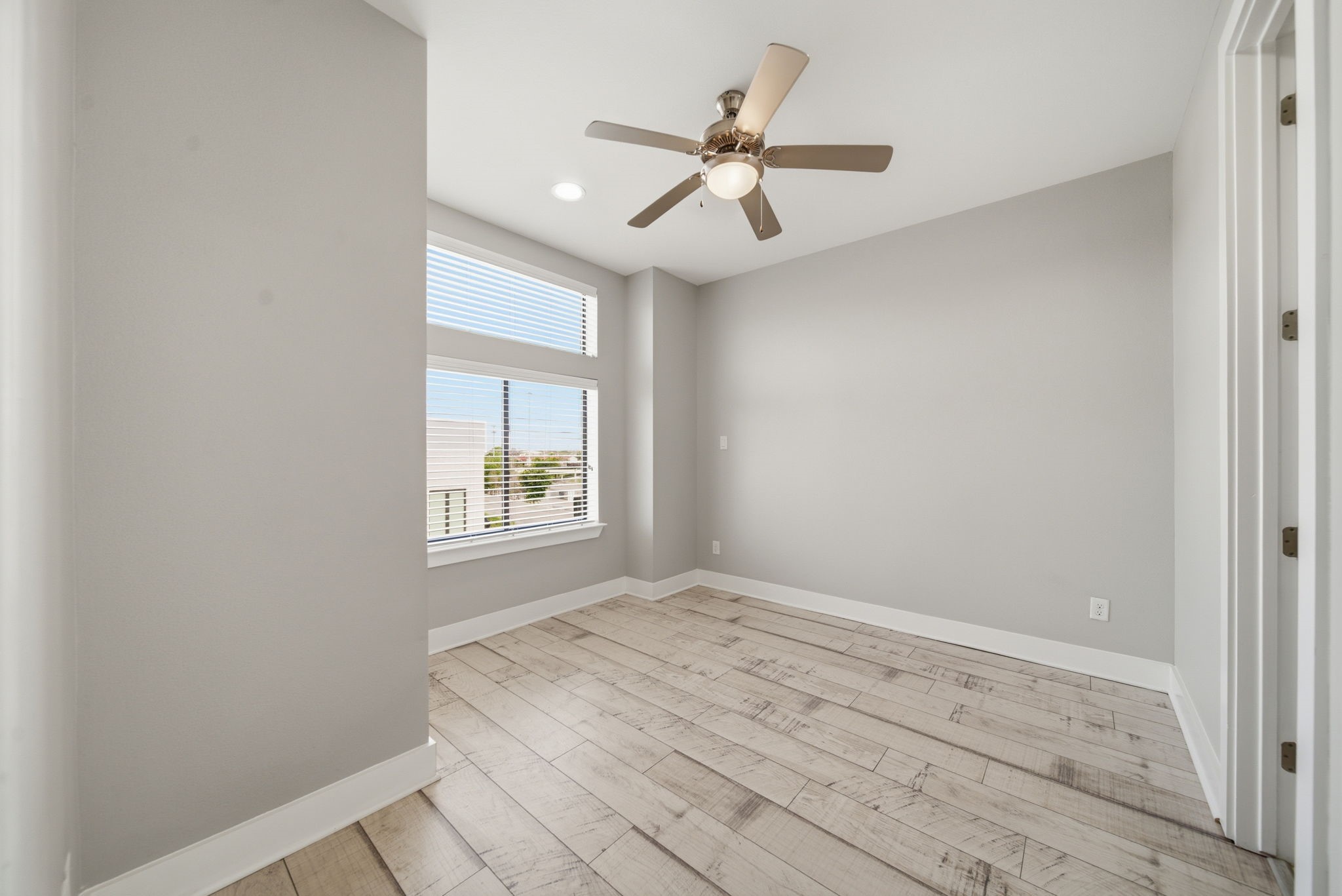 1814 Thompson Street Houston, TX 77007 - Photo 21 of 37 Bright, modern third-floor bedroom featuring light wood flooring and neutral gray tones throughout. Large windows fill the space with natural light, while a ceiling fan adds comfort and functionality. The clean, minimalist design creates an open, airy feel—offering a versatile space that feels both inviting and refined.