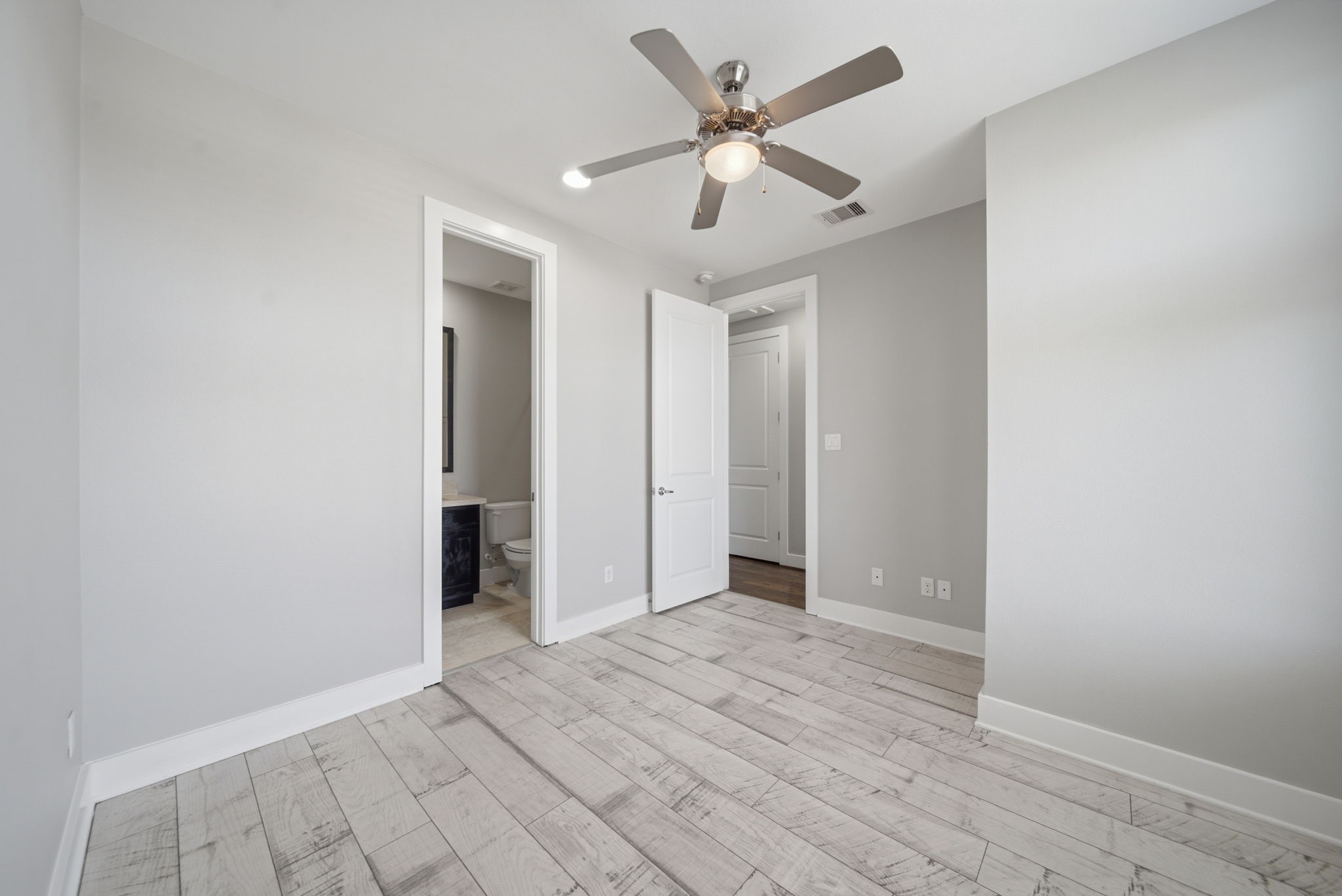 1814 Thompson Street Houston, TX 77007 - Photo 22 of 37 Bright and modern third-floor bedroom featuring light wood flooring, neutral finishes, and a ceiling fan. The space includes a private en-suite bathroom and offers excellent flexibility—ideal for a comfortable bedroom, guest suite, or dedicated home office. Clean, airy, and move-in ready with a contemporary feel.