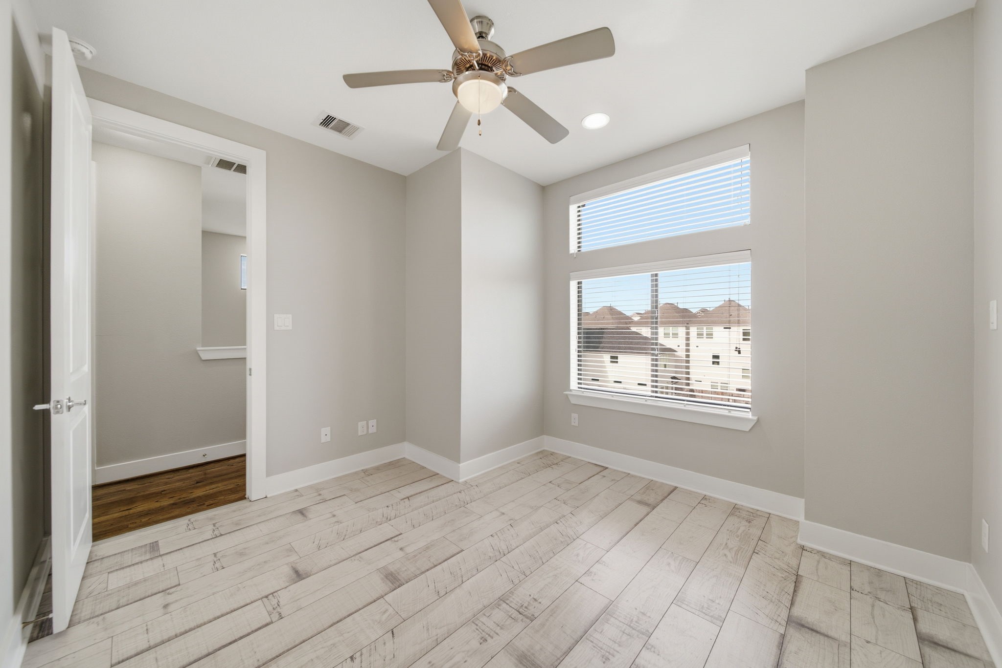 1814 Thompson Street Houston, TX 77007 - Photo 23 of 37 Bright, modern third-floor bedroom featuring light wood flooring, neutral finishes, and a ceiling fan. Large windows with blinds provide excellent natural light, creating an airy, inviting space. Clean and versatile layout ideal for a comfortable bedroom, home office, or flex space.