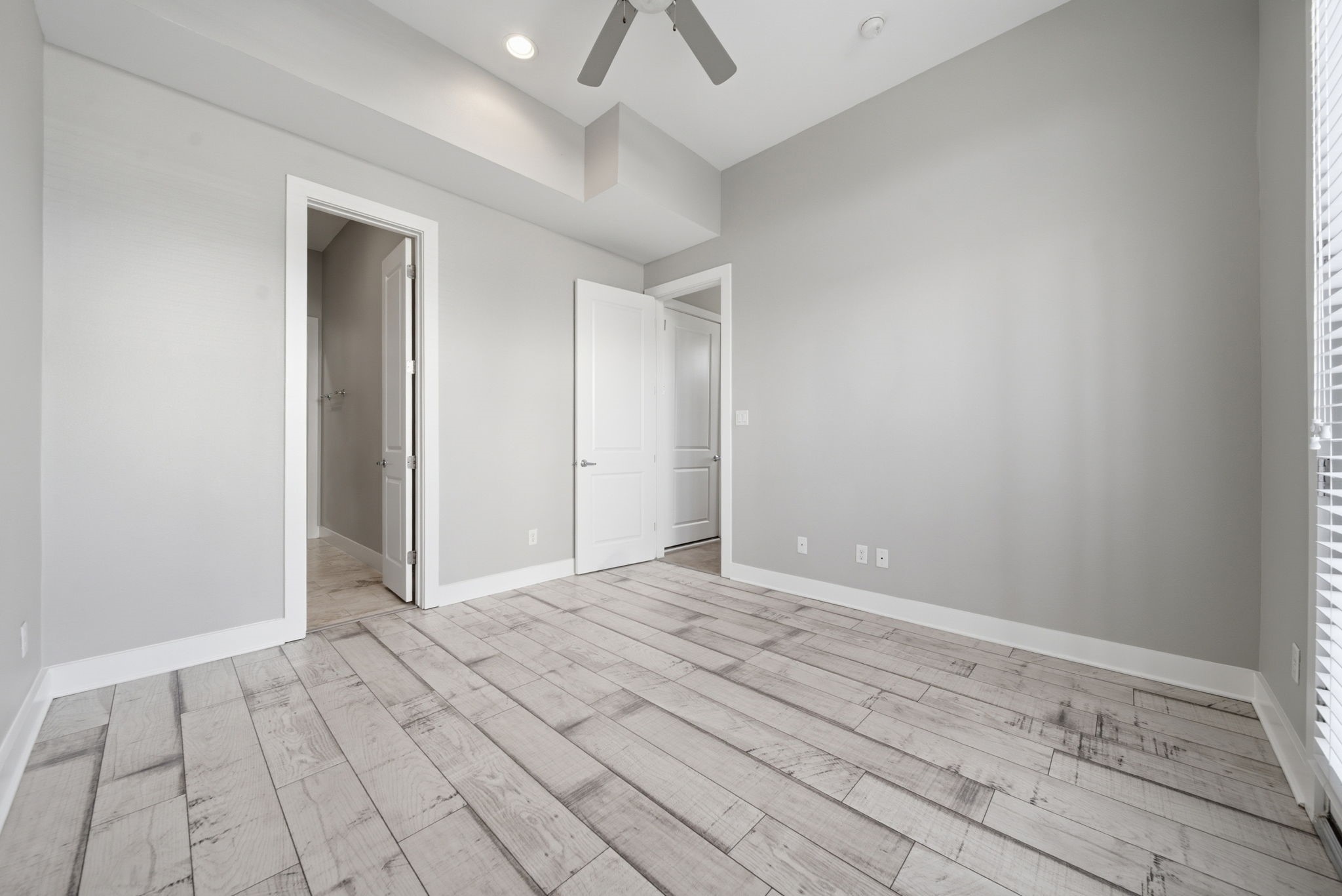 1814 Thompson Street Houston, TX 77007 - Photo 25 of 37 This downstairs bedroom offers a bright, open feel with light gray walls, wide wood-look flooring, and a ceiling fan. High ceilings with recessed lighting enhance the spacious layout, while dual access to the ensuite bathroom and walk-in closet adds exceptional convenience and functionality—perfectly blending comfort and modern design.