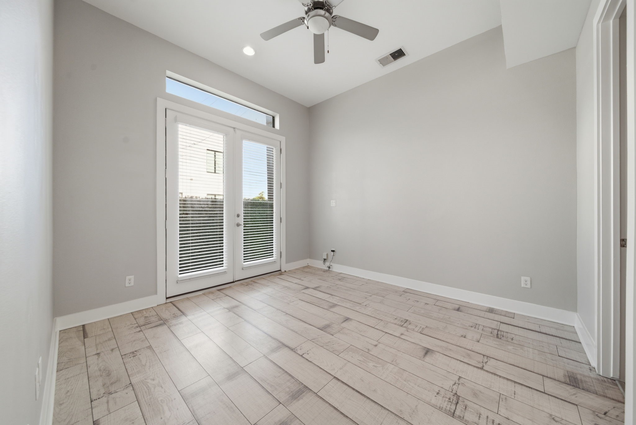 1814 Thompson Street Houston, TX 77007 - Photo 26 of 37 This downstairs bedroom showcases light wood flooring and neutral gray walls for a clean, modern aesthetic. A ceiling fan and expansive glass doors provide excellent natural light and seamless indoor-outdoor access. The space includes a private ensuite bath and walk-in closet, offering both comfort and functionality—ideal as a bedroom, guest suite, or home office.