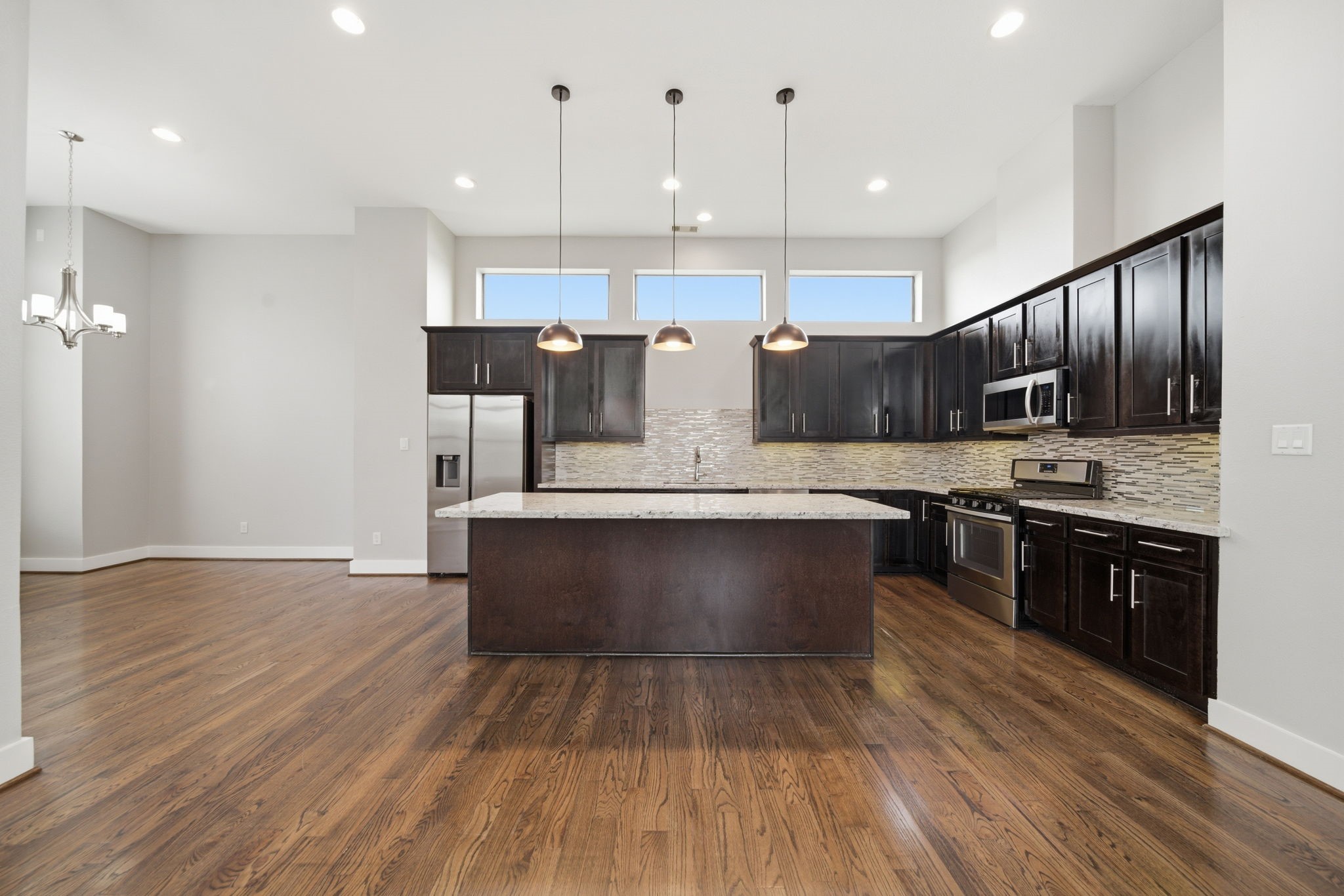 1814 Thompson Street Houston, TX 77007 - Photo 3 of 37 Beautifully designed kitchen featuring dark wood cabinetry, sleek stainless steel appliances, and a large center island ideal for hosting. Soaring ceilings, stylish pendant lighting, and continuous hardwood flooring create a bright, open space perfect for entertaining and daily living.