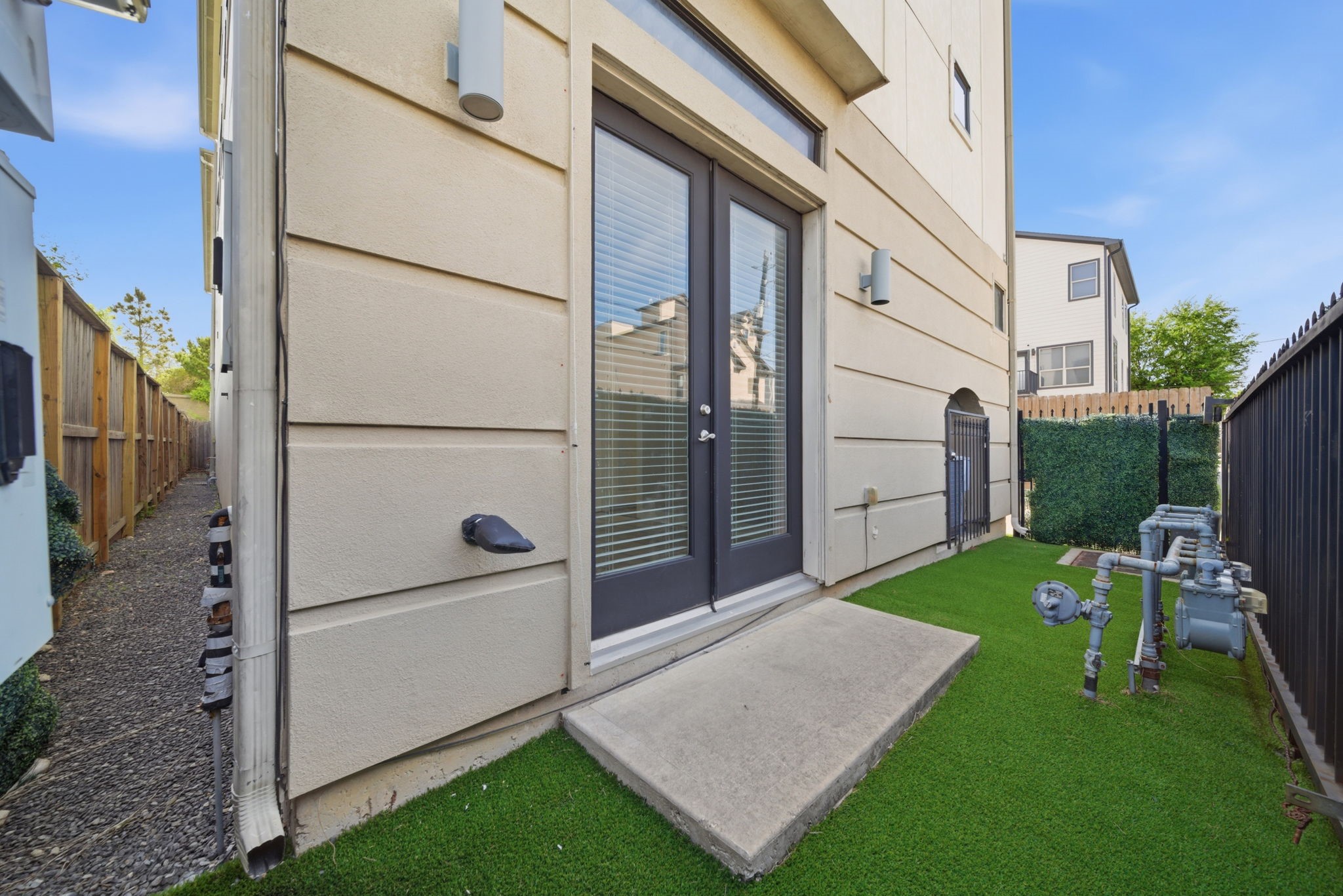 1814 Thompson Street Houston, TX 77007 - Photo 32 of 37 Narrow, low-maintenance side yard featuring artificial turf and a clean, modern design. Framed by a privacy fence and a sleek exterior with double glass doors, the space offers a functional outdoor area with easy upkeep. Conveniently positioned utility access is neatly integrated along the exterior wall, maintaining a streamlined and contemporary feel.