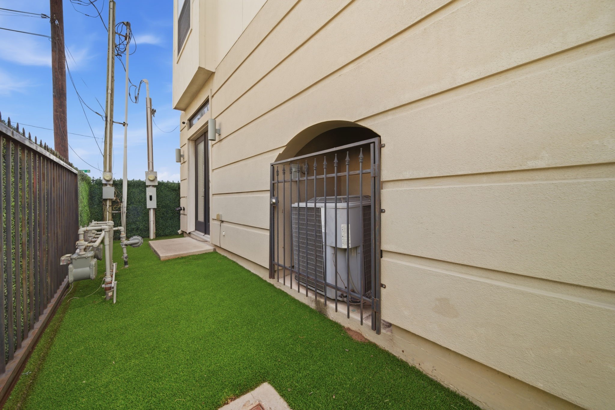 1814 Thompson Street Houston, TX 77007 - Photo 33 of 37 Utility area located along the side of the home featuring low-maintenance artificial turf, HVAC system, and utility meters. Enclosed by a metal fence and exterior wall, offering a clean, functional space that keeps essential systems discreetly organized and easily accessible.