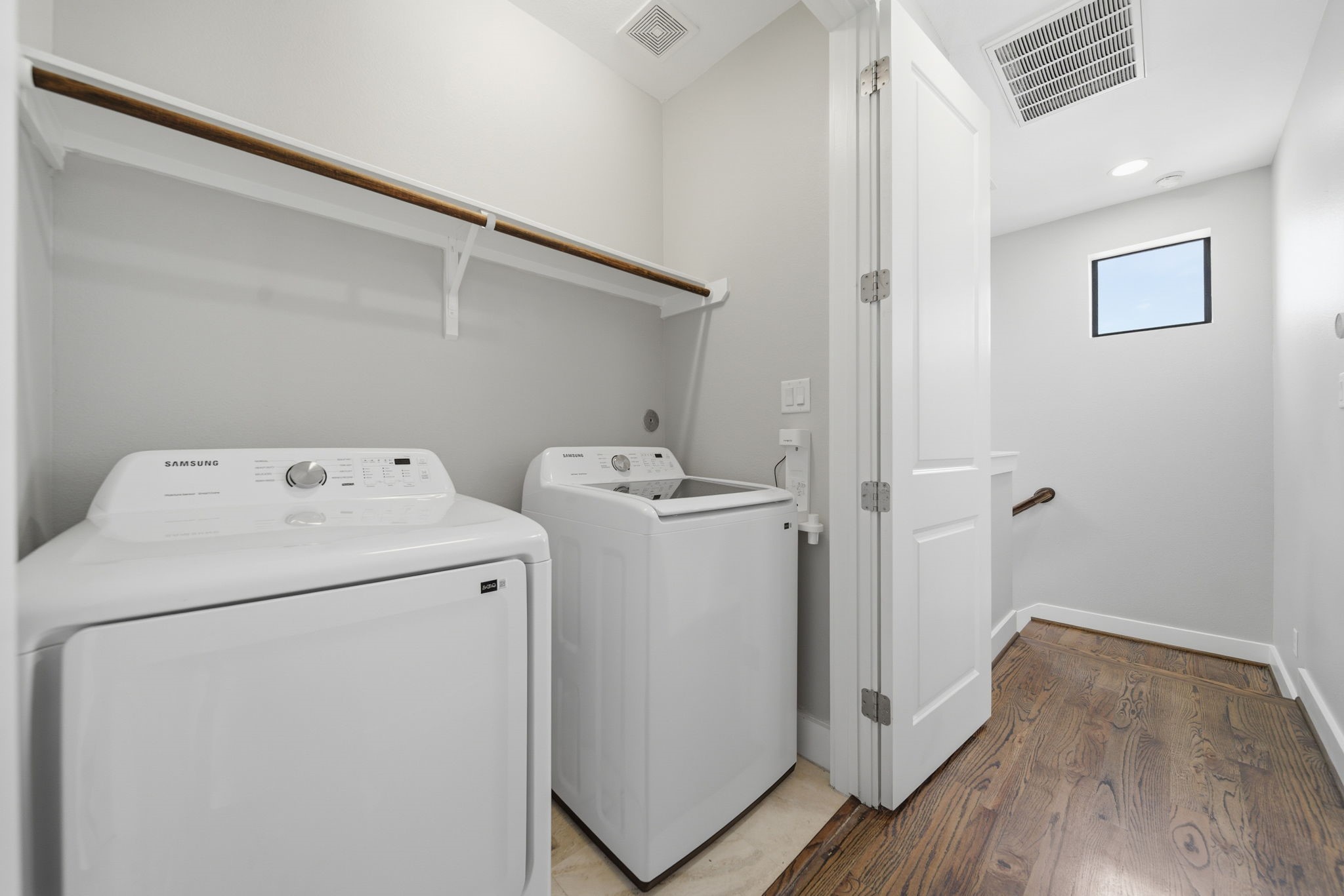 1814 Thompson Street Houston, TX 77007 - Photo 34 of 37 Third-floor laundry area featuring an included washer and dryer for added convenience. The space offers a clean, modern feel with hardwood flooring flowing from the adjacent hallway and a built-in shelf above for additional storage—combining functionality with a bright, well-maintained design.