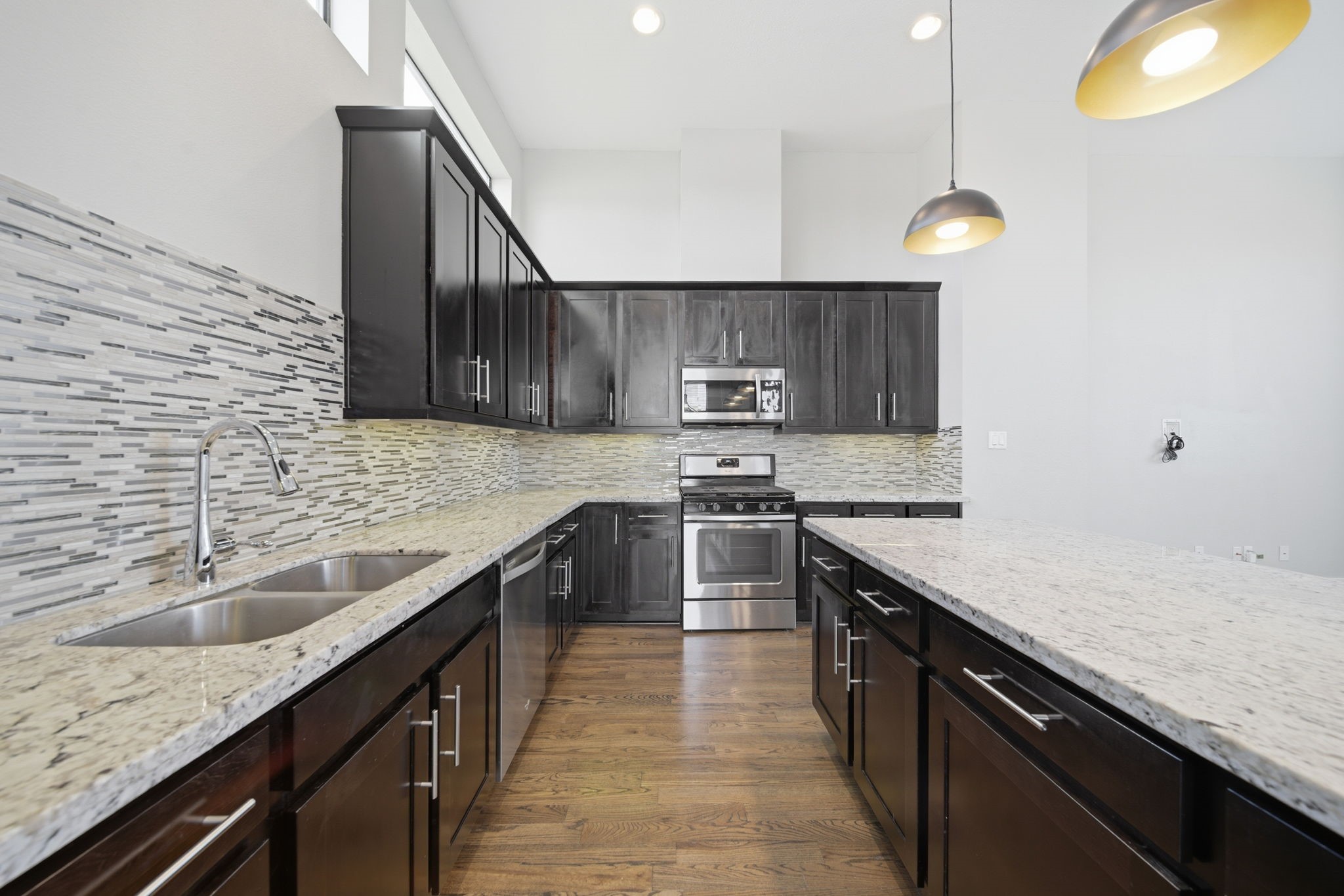 1814 Thompson Street Houston, TX 77007 - Photo 4 of 37 Contemporary kitchen designed to impress, featuring rich dark wood cabinetry, stainless steel appliances, and a stylish tile backsplash. The expansive layout is anchored by a large granite island with elegant pendant lighting—perfect for both everyday living and effortless entertaining.
