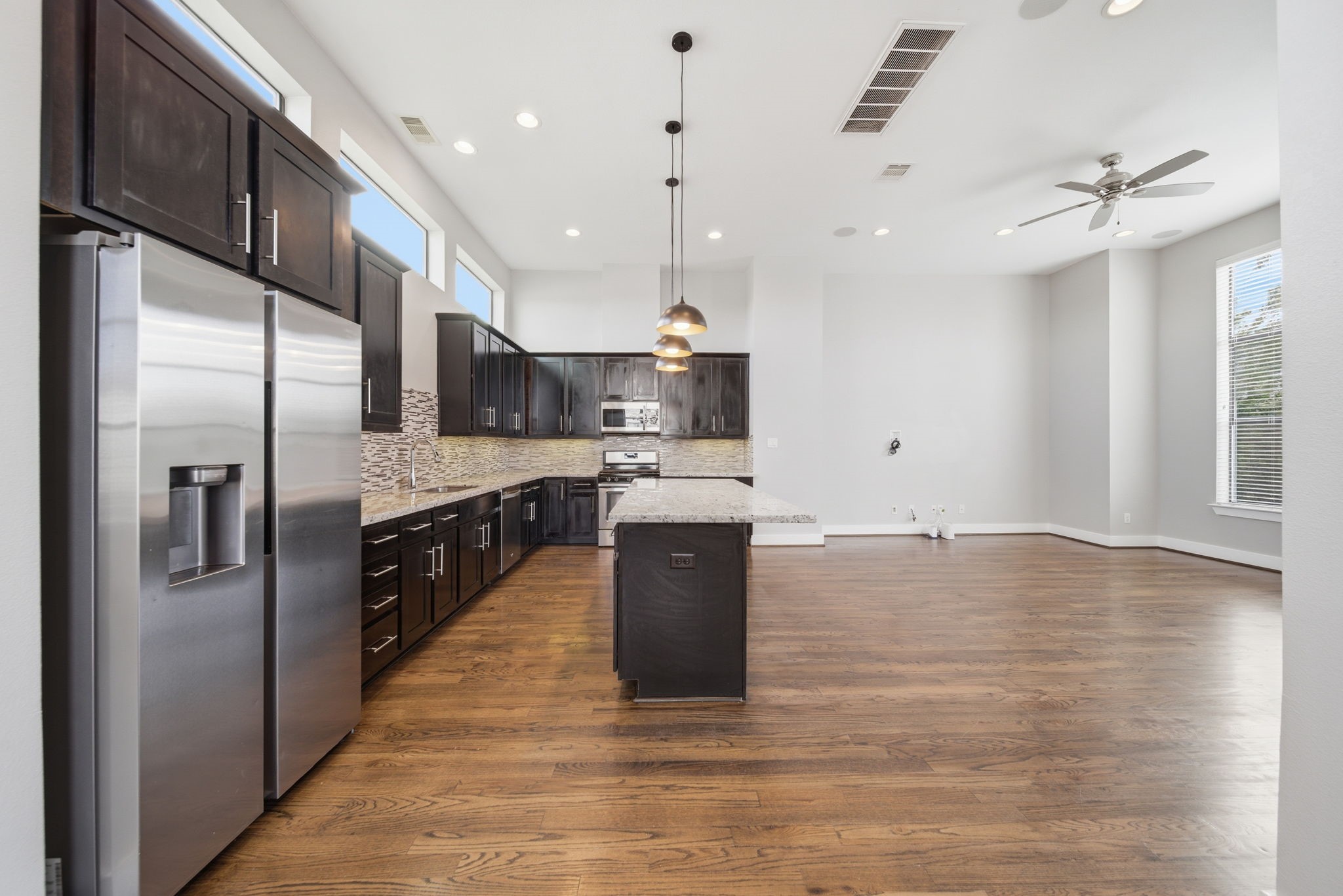 1814 Thompson Street Houston, TX 77007 - Photo 5 of 37 Open-concept kitchen and living area with dark wood cabinetry, stainless steel appliances, and a large island with pendant lighting. High ceilings, hardwood floors, and abundant natural light create a bright, inviting space.