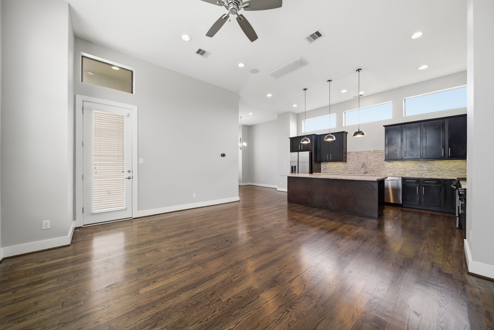 1814 Thompson Street Houston, TX 77007 - Photo 6 of 37 Expansive open-concept living space featuring rich hardwood floors, soaring ceilings, and abundant natural light. The modern kitchen is beautifully appointed with sleek dark cabinetry, a large island, and elegant pendant lighting—offering the perfect blend of style and functionality for everyday living and entertaining.