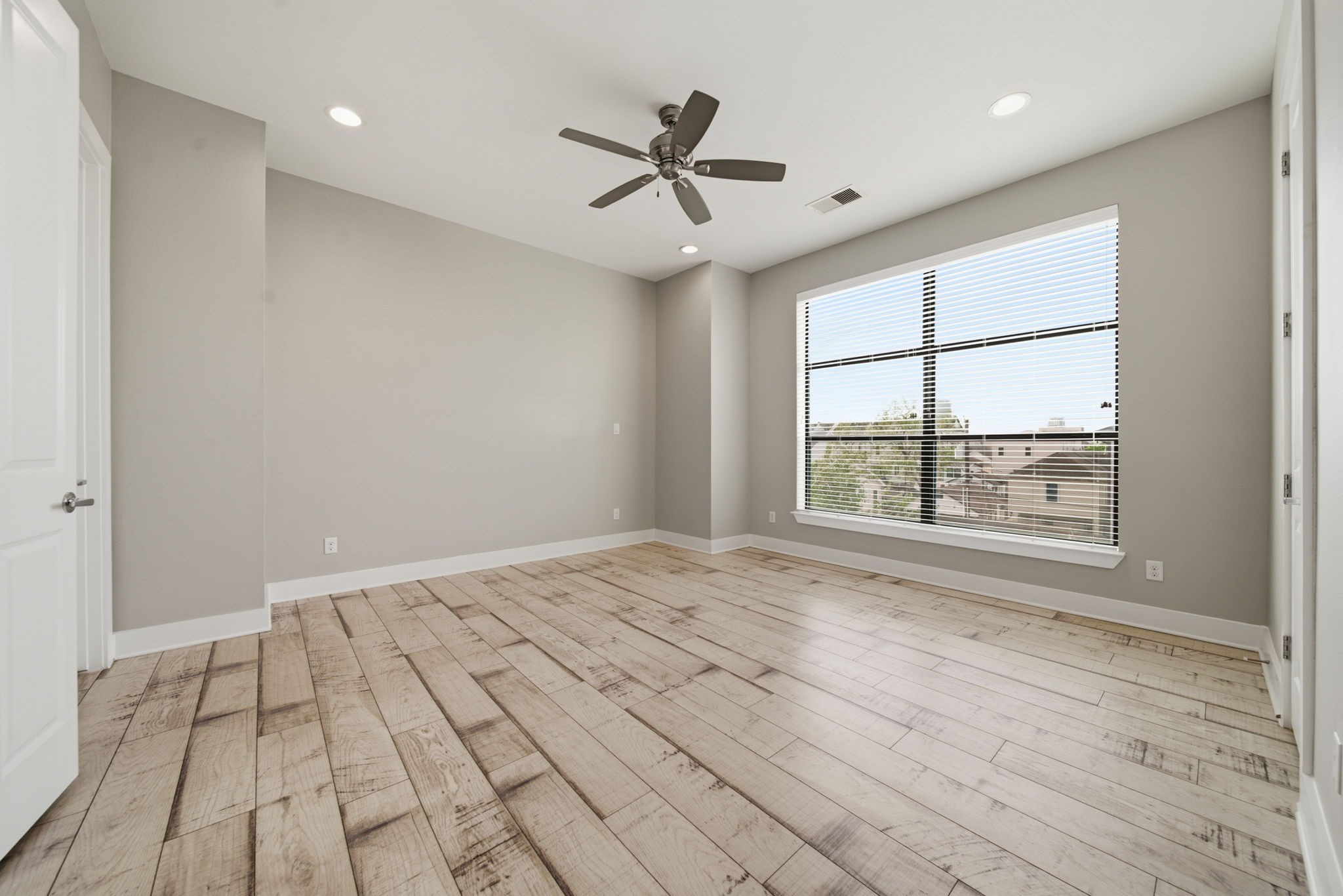 1814 Thompson Street Houston, TX 77007 - Photo 9 of 37 Bright and spacious primary bedroom featuring light wood flooring, neutral tones, and a large window that fills the space with natural light. Enhanced by modern ceiling fan and recessed lighting, the room also offers the convenience of dual walk-in closets—combining comfort, style, and ample storage.
