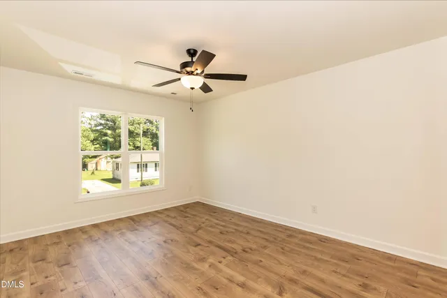 an empty room with wooden floor fan and windows