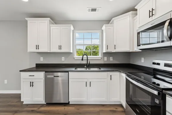 a kitchen with granite countertop white cabinets stainless steel appliances and a window