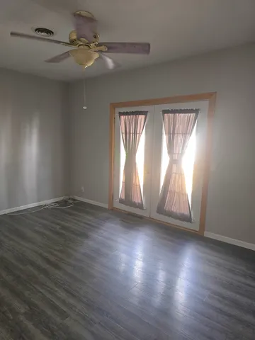 an empty room with wooden floor chandelier fan and windows
