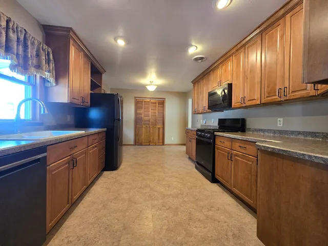a large kitchen with stainless steel appliances granite countertop a stove a sink dishwasher and a refrigerator with wooden cabinets