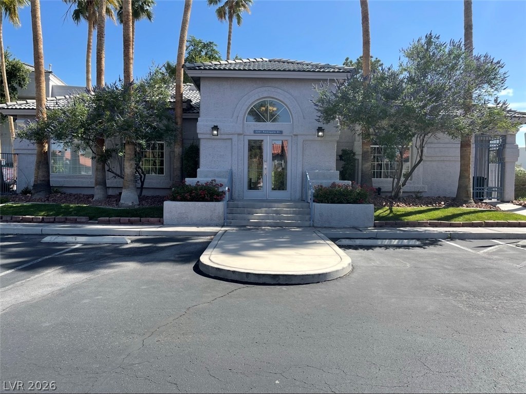 2201 Ramsgate Drive, Unit 915 Henderson, NV 89074 - Photo 10 of 36 A welcoming front entrance with arched windows and lush greenery, set against a backdrop of towering palm trees.
