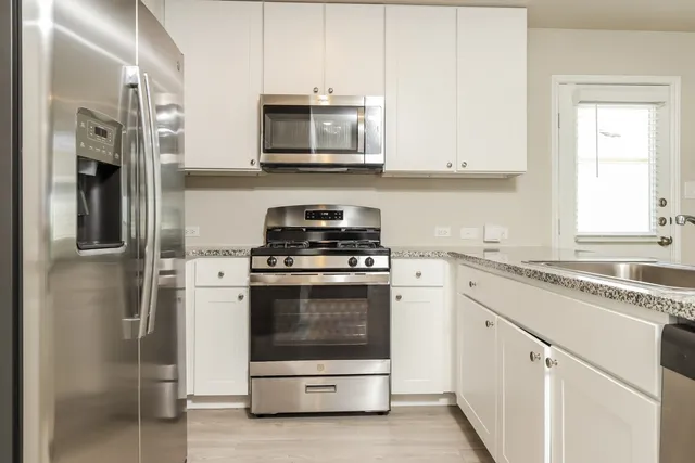 a kitchen with stainless steel appliances granite countertop white cabinets a stove a sink and a white refrigerator