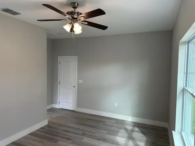 an empty room with wooden floor fan and windows