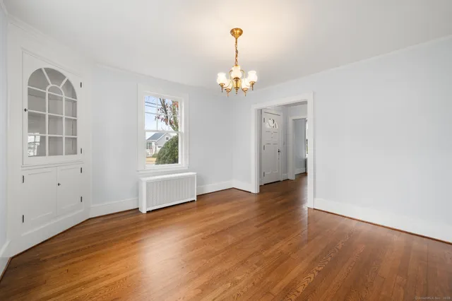 an empty room with wooden floor chandelier and windows