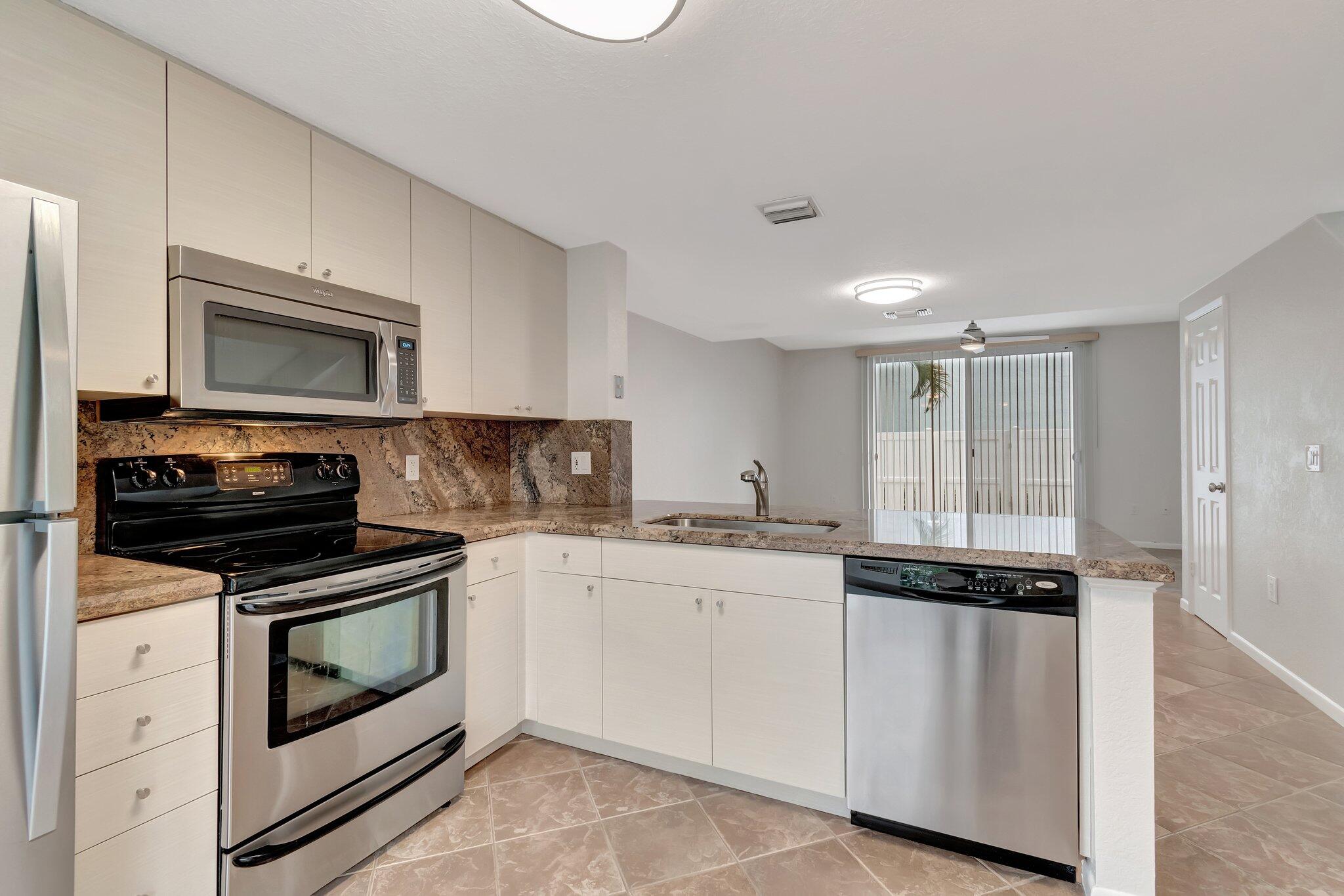 1016 Jeffery Street, Unit 1016 Boca Raton, FL 33487 - Photo 19 of 65 a kitchen with granite countertop white cabinets and stainless steel appliances