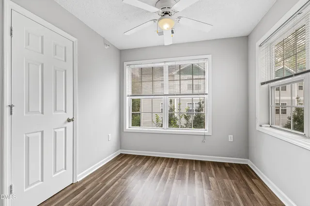 an empty room with wooden floor fan and windows