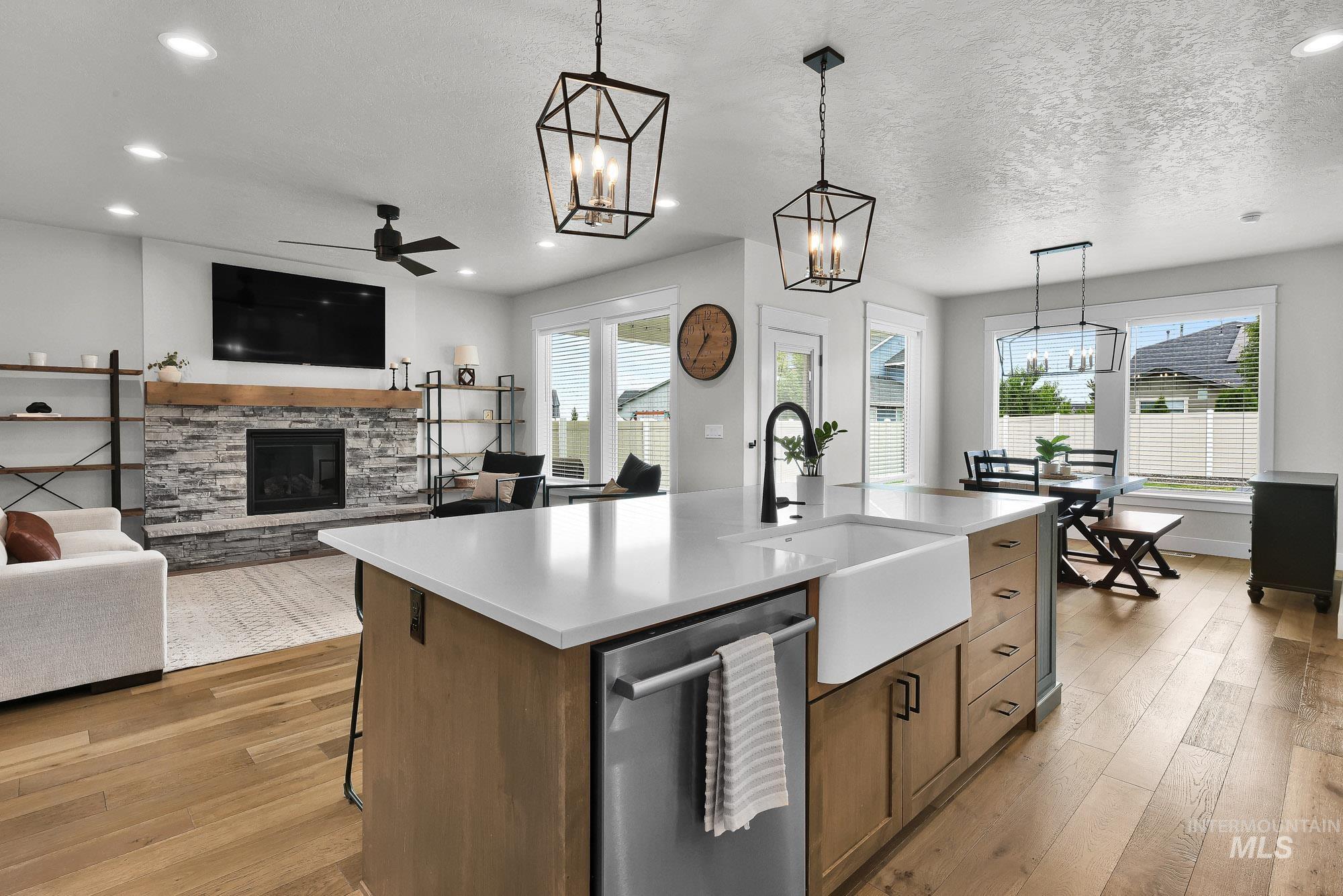 5676 East Zaffre Ridge Street Boise, ID 83716 - Photo 15 of 50 Open-concept living space featuring wood-finish flooring, a stone fireplace with a wood mantle, and a kitchen island with a farmhouse sink