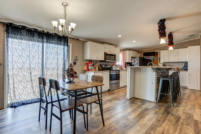 a kitchen with stainless steel appliances granite countertop a refrigerator a stove a sink a dining table and chairs with wooden floor