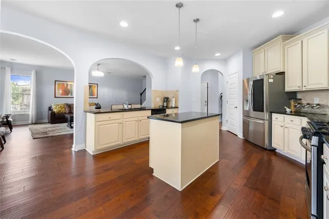 a kitchen with stainless steel appliances kitchen island granite countertop a stove a sink a refrigerator and a wooden floor