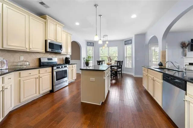 a kitchen with stainless steel appliances granite countertop wooden floors a stove a sink and white cabinets