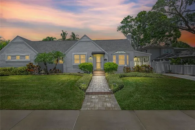 a view of a brick house with a big yard plants and large trees