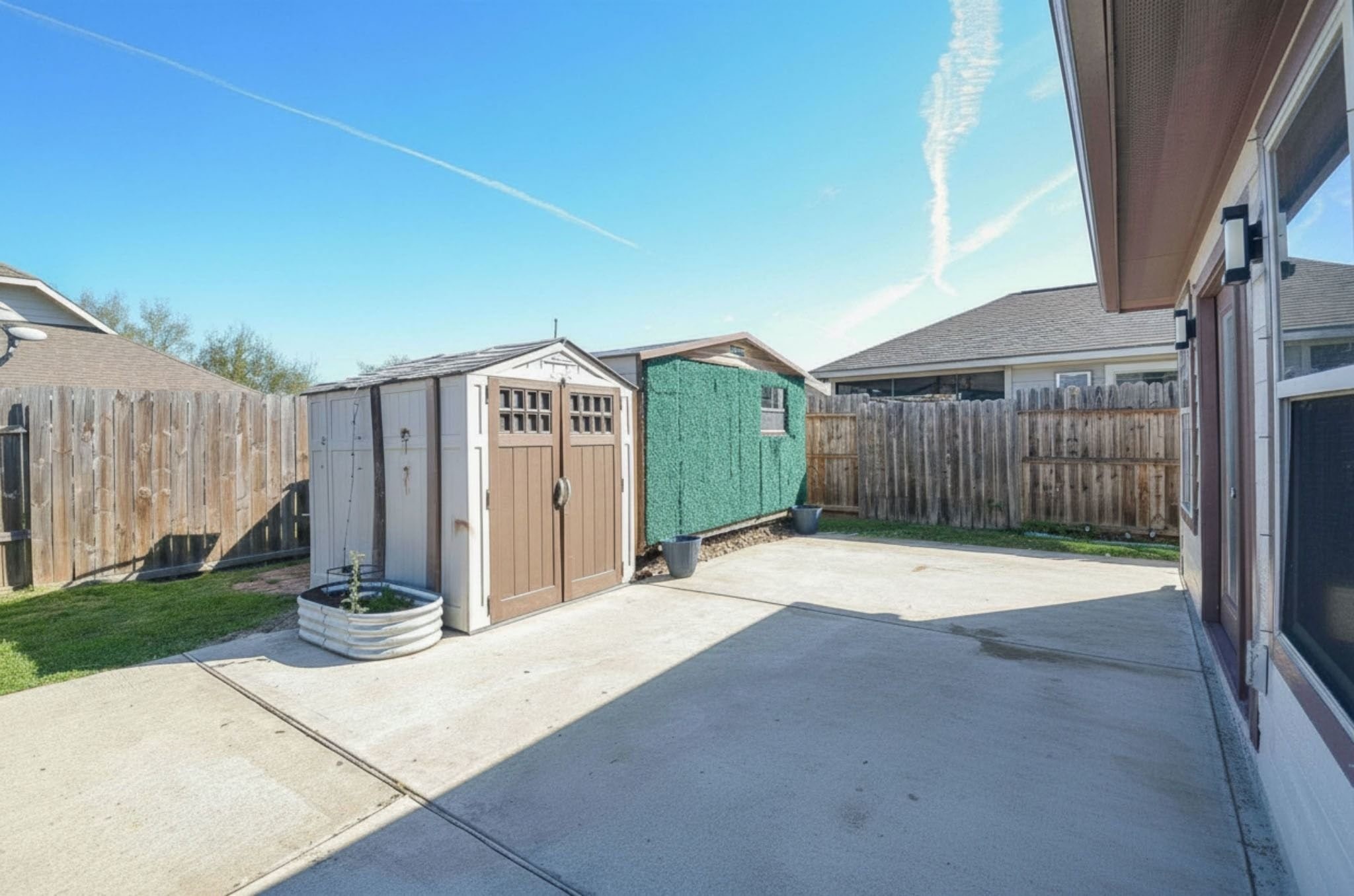 5411 Rio Drive Baytown, TX 77521 - Photo 27 of 30 The backyard features a large concrete patio area with two storage sheds, surrounded by a wooden privacy fence. Ideal for outdoor activities and storage.