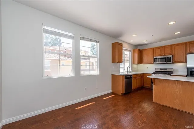 a kitchen with stainless steel appliances granite countertop a stove top oven a sink dishwasher and a refrigerator with wooden floor