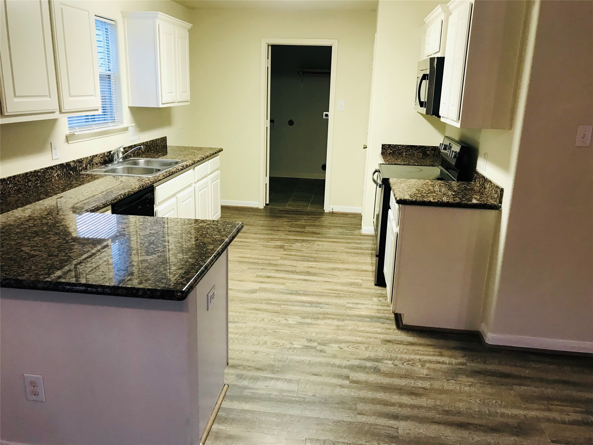 28854 Llano River Loop Spring, TX 77386 - Photo 5 of 19 This kitchen features sleek granite countertops, white cabinetry, and stainless steel appliances. It has a practical layout with ample counter space, natural light from a window, and a modern, wood-look floor.