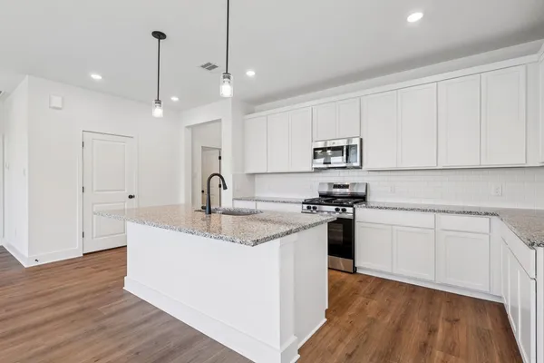a kitchen with stainless steel appliances granite countertop a sink stove and white cabinets with wooden floor