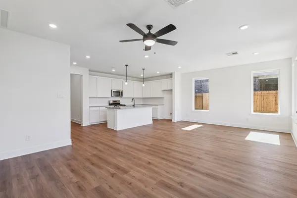 a view of an empty room with wooden floor and a kitchen