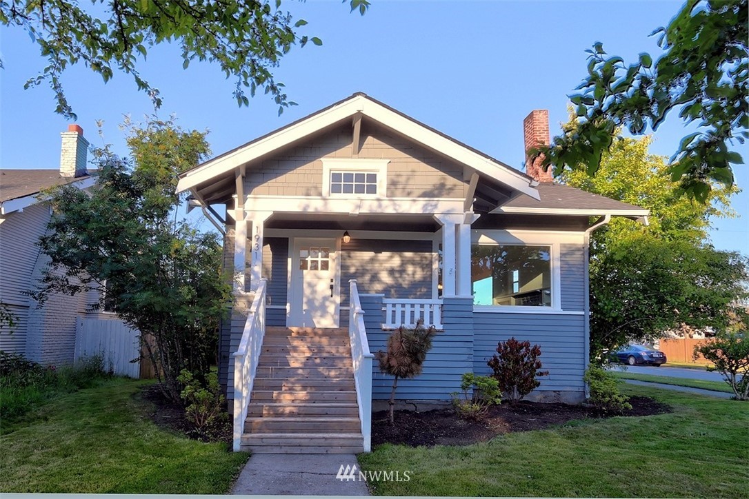 a view of a house with brick walls and a yard with plants and large trees