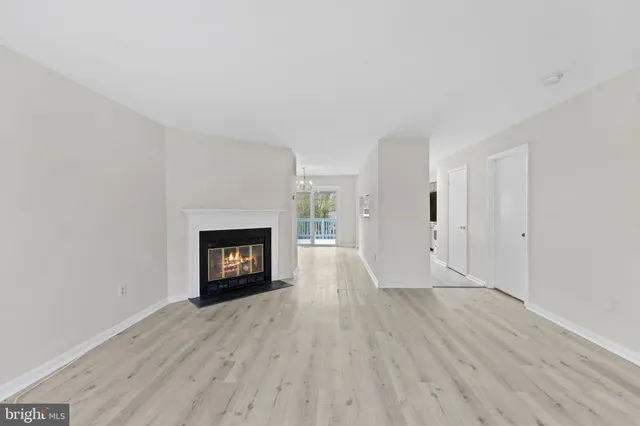 a view of an empty room with wooden floor fire place and a window