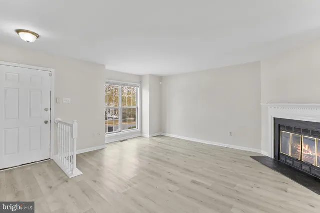 a view of an empty room with wooden floor fireplace and a window