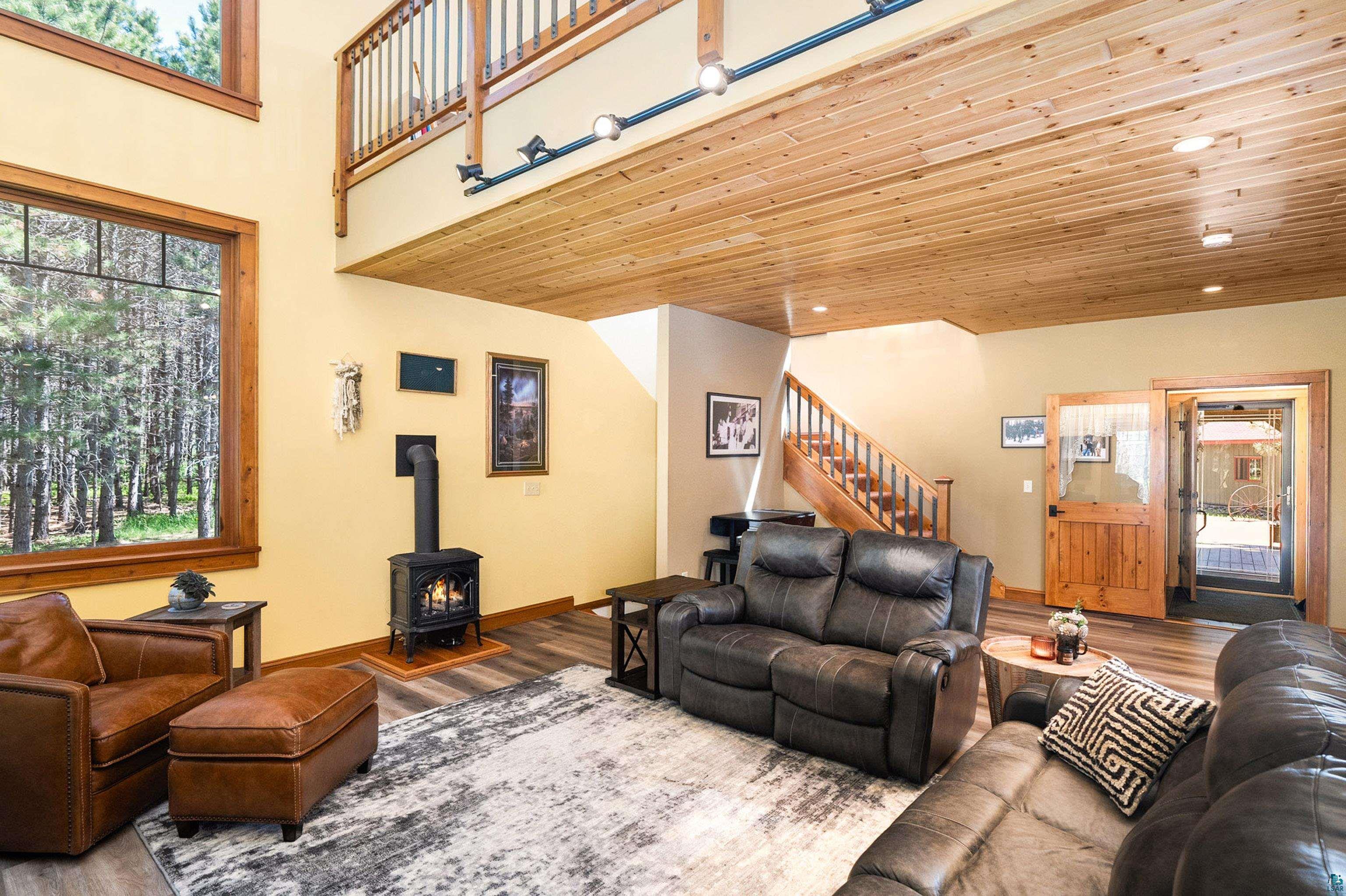 75 East Stark Road Esko, MN 55733 - Photo 17 of 87 Spacious living area featuring a prominent wood-burning stove, large windows with natural wood trim, wood-finish flooring, and a natural wood plank ceiling
