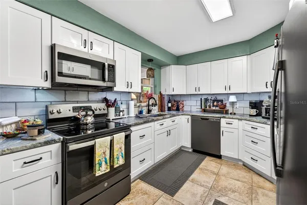 a kitchen with stainless steel appliances granite countertop grey cabinets a stove a sink and dishwasher