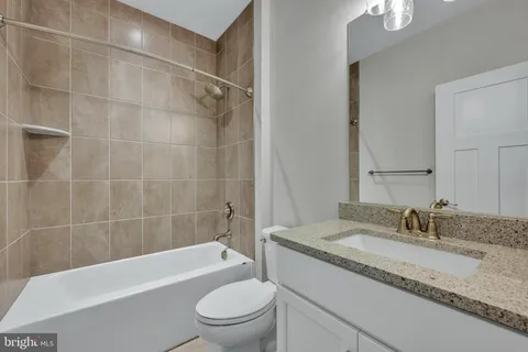 a bathroom with a granite countertop bathtub shower sink vanity mirror and toilet