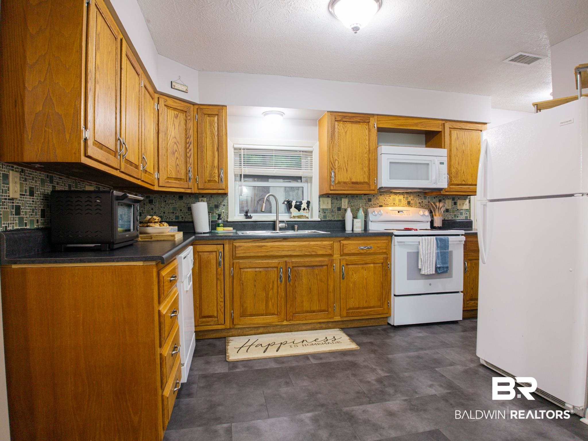 1563 Valencia Drive Lillian, AL 36549 - Photo 3 of 27 Kitchen featuring white appliances, dark countertops, tasteful backsplash, brown cabinetry, and a textured ceiling