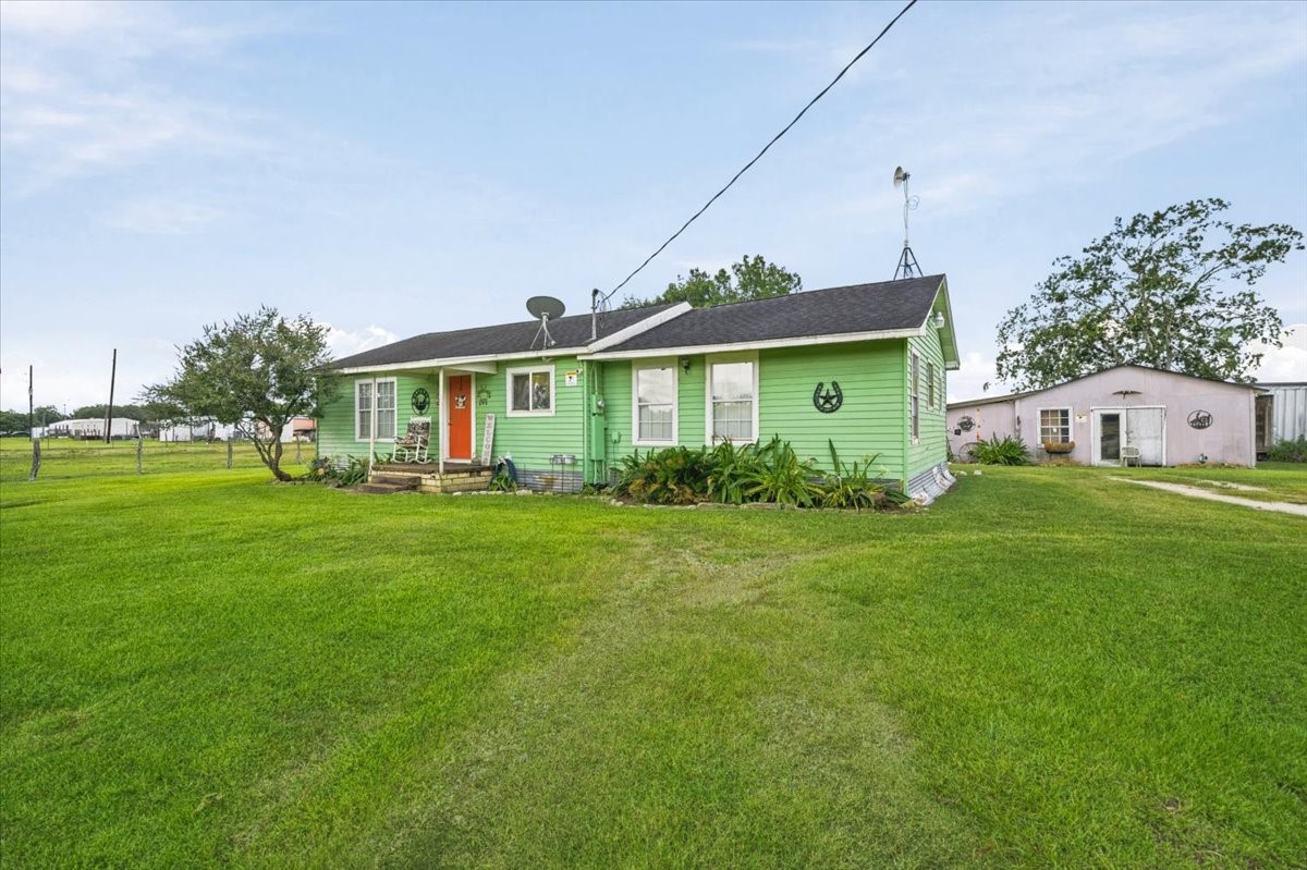 765 Norcross Road Wallis, TX 77485 - Photo 6 of 42 Charming ranch-style home with a cozy front porch, surrounded by a spacious, well-maintained lawn. A separate outbuilding adds extra utility in a peaceful, rural setting.
